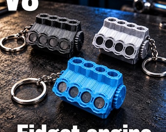 Könnte beinhalten: Drei V8-Motor-Fidget-Schlüsselanhänger in Schwarz, Silber und Blau. Jeder Schlüsselanhänger zeigt ein detailliertes Motorblockmodell mit einem kreisförmigen Zahnrad an der Seite und einem Metallring, der an einer kurzen Kette befestigt ist. Der Text V8 Fidget engine ist sichtbar.