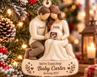 May include: A clear acrylic Christmas ornament featuring a sculpted couple with the names David and Emily printed on their shirts. The couple holds a small ultrasound image. The base text reads We're Expecting! Baby Carter Arriving 2027.