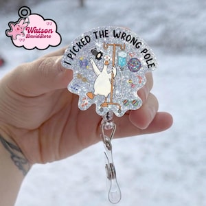 May include: A glittery badge reel with the phrase "I PICKED THE WRONG POLE." The design features a cartoon goose in a nurse's hat, holding an IV drip. Additional graphics include a disco ball and musical notes.