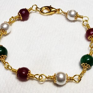 May include: A gold wire wrapped bracelet with red, green, and white beads. The beads are accented with gold filigree.