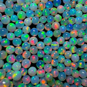 May include: A collection of numerous round, translucent white opal gemstones arranged closely together. Each stone displays a vibrant play-of-color, featuring flashes of neon green, bright orange, and electric blue against a milky base.