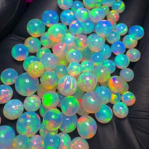 以下が含まれることがあります： 青、緑、オレンジなど、さまざまな色を示す、虹色のオパール球のコレクション。球は丸く滑らかで、研磨された外観をしています。オパールはさまざまなサイズで、暗い表面に散らばっています。
