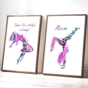 May include: Two framed art prints featuring watercolor dancers in motion. One print reads "Dance like nobody's watching!" The other print has the name "Maeve." The dancers are depicted in shades of purple, green, and blue.