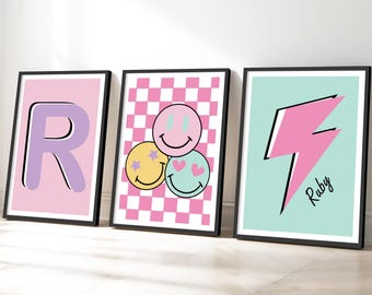 May include: Three framed art prints. The first features a pink background with a large letter "R" in purple. The second has a pink and white checkered pattern with three smiley faces. The third has a pink lightning bolt with the name "Ruby".