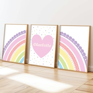 May include: Three framed art prints with a rainbow theme. The prints feature pastel rainbows, polka dots, and a pink heart with the name "Charlotte". The frames are a light brown colour.
