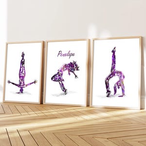May include: Three framed art prints featuring watercolor illustrations of a dancer in various poses. The dancer is depicted in shades of purple and white. The middle print has the name "Penelope" in cursive. The frames are light brown.
