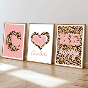Könnte beinhalten: Drei gerahmte Kunstdrucke. Der erste zeigt einen rosa Hintergrund mit einem Leopardenmuster "C". Der zweite hat ein rosa Herz mit Leopardenmuster und dem Namen "Charlotte". Der dritte sagt "BE happy" auf einem Leopardenmuster-Hintergrund.