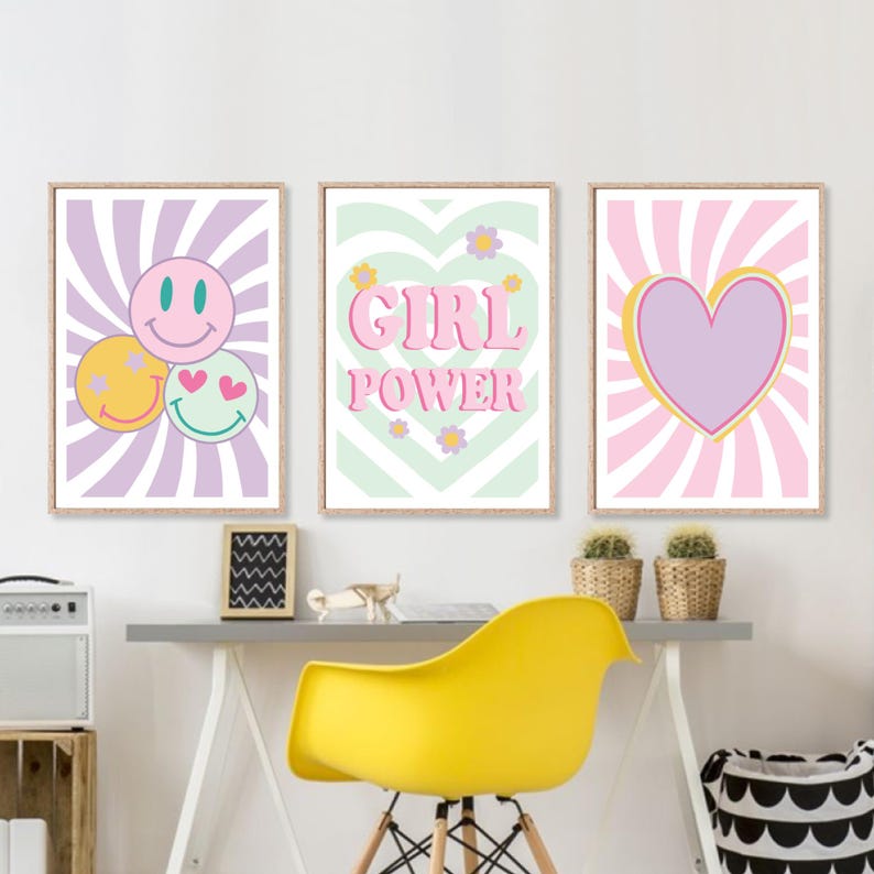 May include: Three framed wall art prints with a retro theme. One print features smiley faces, another reads "GIRL POWER," and the third has a heart design. The prints are in pastel colors with a wooden frame.