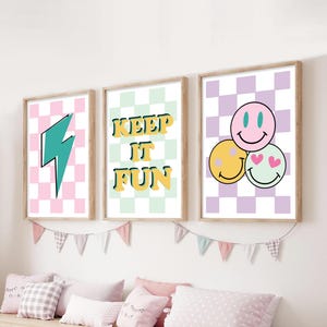 Può includere: Tre stampe artistiche incorniciate con un tema retrò. Una stampa presenta un fulmine turchese su uno sfondo a scacchi rosa e bianco. La seconda stampa dice "KEEP IT FUN" in giallo e verde. La terza stampa ha tre faccine sorridenti.