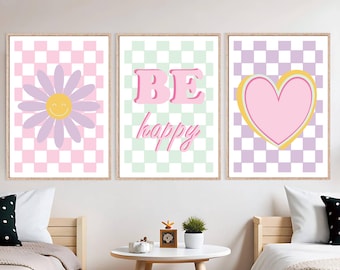 May include: Three framed wall art prints with a cheerful theme. The prints feature a daisy, the words "BE happy", and a heart, all set against a checkered background in pastel colors. The frames are a light wood color.