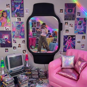 Puede incluir: Una habitación decorada con una estética retro, con un gran espejo negro en forma de reloj. Las paredes están adornadas con carteles, fotos y una tira de LED de colores. También se ve un sofá inflable rosa y una configuración de computadora vintage.