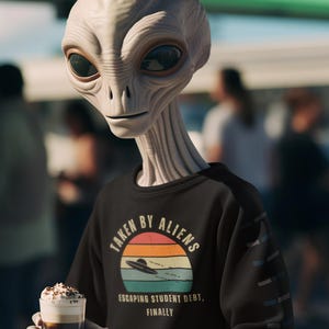 Op de afbeelding: Een alien met een groot hoofd en donkere ogen draagt een zwarte trui met de tekst "TAKEN BY ALIENS" boven een retro zonsondergangontwerp en een vliegende schotel. De alien houdt een glas koffie vast.