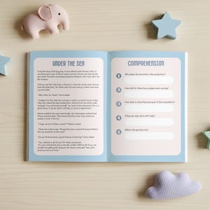 May include: An open children's book with text and comprehension questions, titled "Under the Sea." The book is light blue with white text and illustrations. A pink elephant and blue star-shaped decorations are on the table.