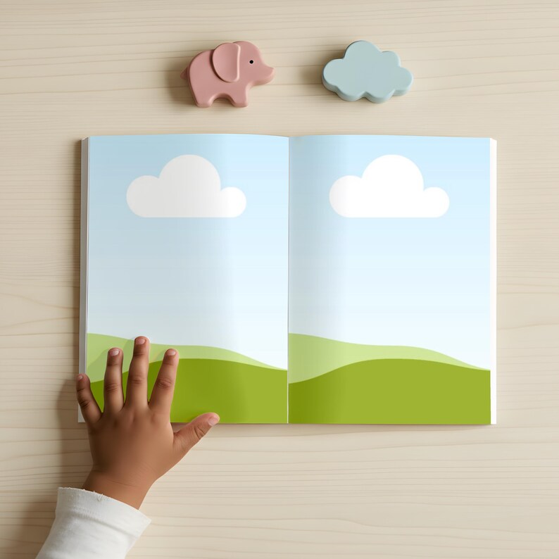 May include: An open book with a blue sky and green landscape illustration, featuring white cloud shapes. A pink elephant and a blue cloud-shaped wooden toy are above the book. A child's hand is touching the book.