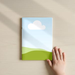 May include: A children's book with a cover featuring a blue sky, a white cloud, and green rolling hills. The book is on a light wood surface, with a child's hand partially visible.