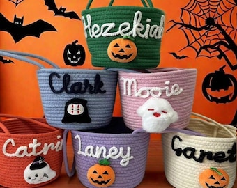 May include: Six handmade Halloween rope baskets in various colours. Each basket has a name in white script, a Halloween character, and a pumpkin. The colours include green, blue, pink, orange, purple, and cream, perfect for trick-or-treating.