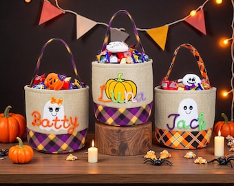May include: Three Halloween treat bags with handles, filled with sweets. Each bag has a different design: a ghost with the name "Batty", a pumpkin with the name "Luna", and a ghost with the name "Jack". The bags have a plaid pattern.