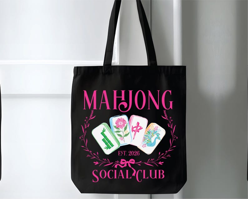 Puede incluir: Bolso tote negro con texto e ilustraciones rosas. Las palabras "MAHJONG SOCIAL CLUB" se muestran, junto con "EST. 2026". El dise&ntilde;o incluye cuatro fichas de Mahjong y una corona floral.