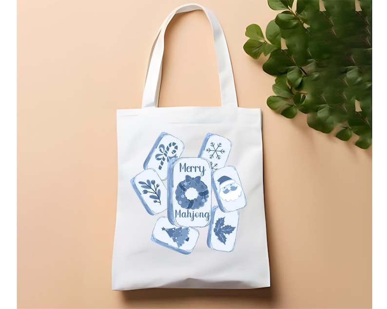 May include: White tote bag featuring blue and white illustrations of Mahjong tiles with holiday-themed designs. The text "Merry Mahjong" is displayed in the center. The bag has two white handles.