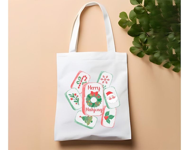 May include: White tote bag featuring a festive design. The bag displays colorful illustrations of Christmas-themed Mahjong tiles. The central tile reads "Merry Mahjong" with a wreath. Other tiles show a candy cane, snowflake, Santa, and more.