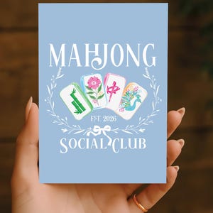 Puede incluir: Una tarjeta azul claro con las palabras "MAHJONG SOCIAL CLUB" en blanco. La tarjeta presenta cuatro fichas de Mahjong con varios dise&ntilde;os, rodeadas por una corona floral blanca. Tambi&eacute;n est&aacute; presente el texto "EST. 2026".