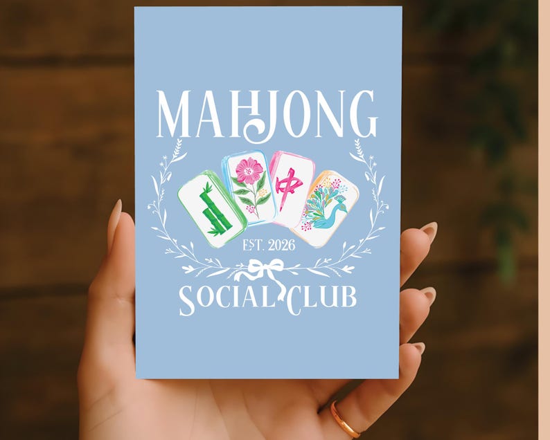 Puede incluir: Una tarjeta azul claro con las palabras "MAHJONG SOCIAL CLUB" en blanco. La tarjeta presenta cuatro fichas de Mahjong con varios dise&ntilde;os, rodeadas por una corona floral blanca. Tambi&eacute;n est&aacute; presente el texto "EST. 2026".