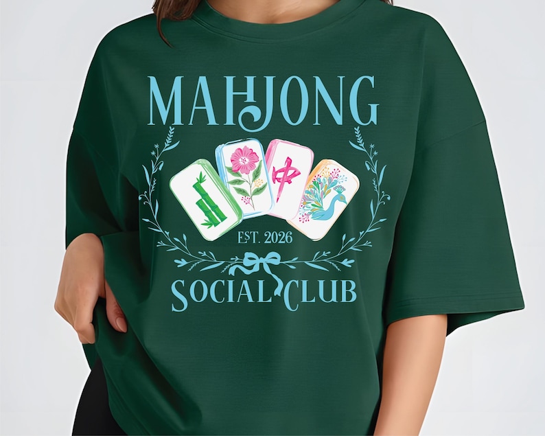 Puede incluir: Sudadera verde oscuro con las palabras "MAHJONG SOCIAL CLUB" en azul claro. El dise&ntilde;o incluye cuatro fichas de Mahjong con ilustraciones florales y de aves, y el texto "EST. 2026".