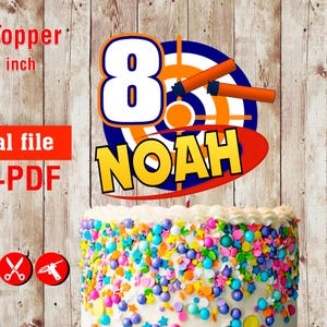 May include: A birthday cake with a custom cake topper. The topper has a target design, the number 8, orange darts, and the name "NOAH". The cake is decorated with colorful sprinkles. The cake topper is 17.78 cm.