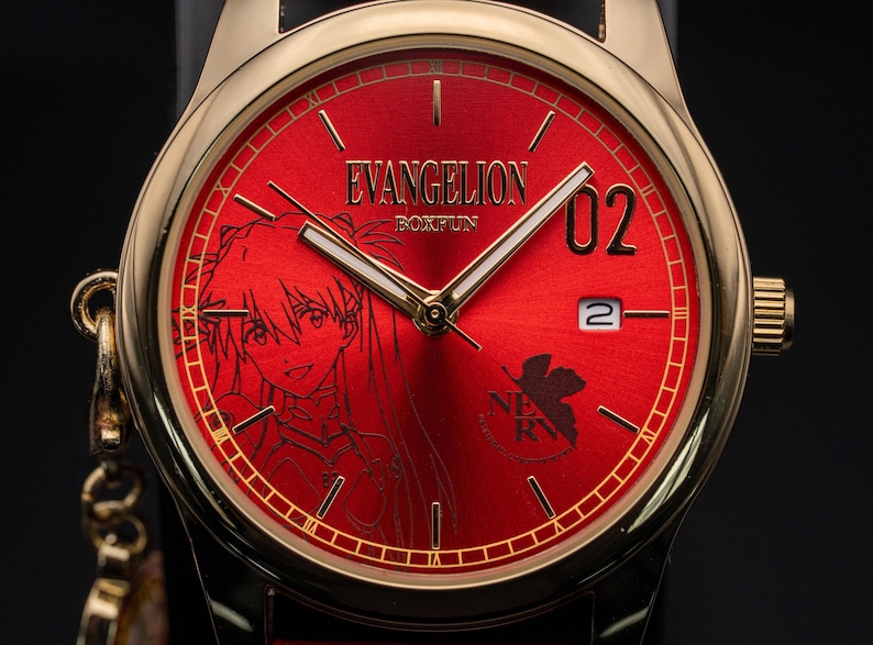 Pu&ograve; includere: Orologio da polso color oro con quadrante rosso con un'illustrazione di un personaggio anime e la scritta "EVANGELION BOXFUN". L'orologio ha lancette dorate e un datario. Il cinturino &egrave; nero.