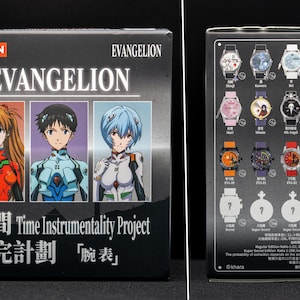 Pu&ograve; includere: Una scatola nera con la scritta "EVANGELION" e illustrazioni di personaggi. La scatola mostra anche testo giapponese e la frase "Time Instrumentality Project". Il retro della scatola mostra immagini di vari orologi con diversi design.