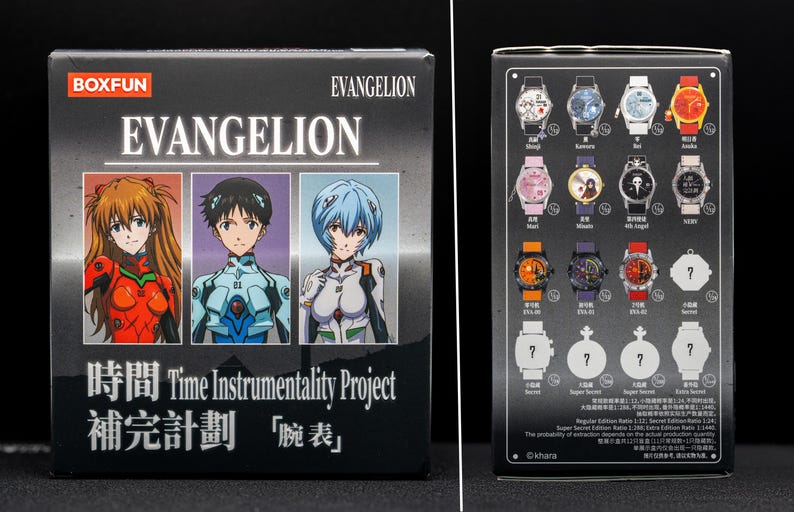 Pu&ograve; includere: Una scatola nera con la scritta "EVANGELION" e illustrazioni di personaggi. La scatola mostra anche testo giapponese e la frase "Time Instrumentality Project". Il retro della scatola mostra immagini di vari orologi con diversi design.
