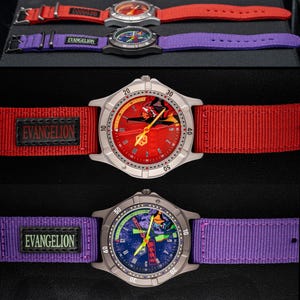 Pu&ograve; includere: Tre orologi da polso con quadranti e cinturini colorati. L'orologio in alto ha cinturino e quadrante rossi, l'orologio centrale ha cinturino viola e quadrante blu, e l'orologio in basso ha quadrante e cinturino rossi. Il testo "EVANGELION" &egrave; sui cinturini.