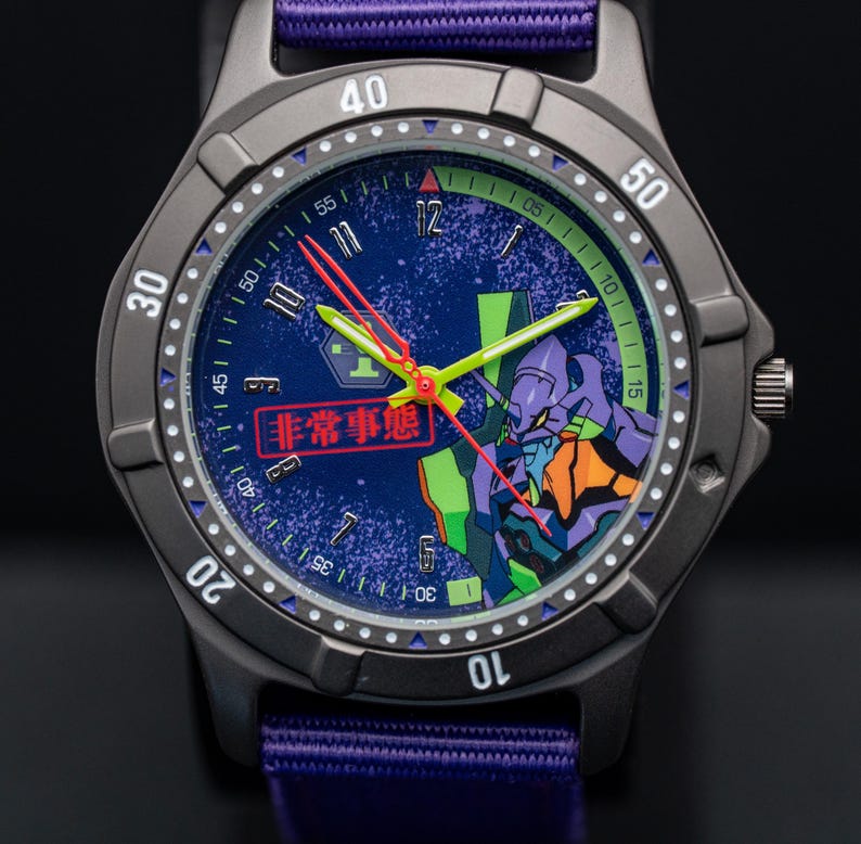 Pu&ograve; includere: Un orologio da polso grigio scuro con cinturino in nylon viola. Il quadrante blu presenta una grafica di un personaggio viola e verde. Le lancette dell'orologio sono rosse e verdi. Il testo "非常事態" &egrave; visibile.