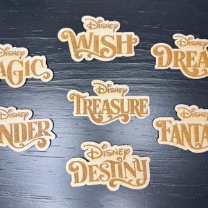May include: Eight wooden Disney-themed ornaments with gold lettering. The ornaments feature the words "Magic", "Wish", "Dream", "Treasure", "Wonder", "Fantasy", "Destiny", and "Disney".