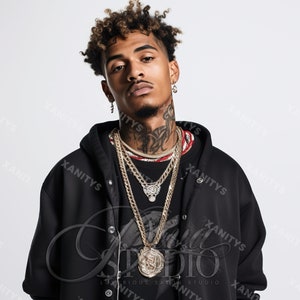 May include: A young man with curly brown hair wearing a black hooded sweatshirt with a large silver pendant necklace. The pendant features a detailed design and is surrounded by multiple gold chains.