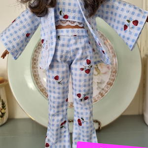 Puede incluir: Un conjunto de muñeca de vichy azul y blanco con estampado de fresa. El conjunto incluye una chaqueta, un top corto y pantalones. Los pantalones tienen un estilo de pierna ancha. El conjunto es para una muñeca.  "pdf pattern Example of Use"