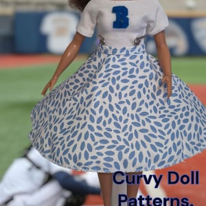 May include: A white doll wearing a white t-shirt with a blue letter "B" on the front and a blue and white patterned skirt. The doll is standing on a wooden platform with a baseball field in the background. The text "Curvy Doll Patterns. ETSY.com" is visible in the bottom right corner of the image.