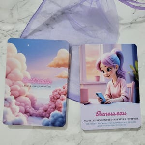 May include: A deck of CutOracle cards with a dreamy aesthetic. One card features a cartoon woman with purple and blue hair, holding a phone. The text "Renouveau" is displayed, along with French text. The other card shows pink clouds and the text "CutOracle LES CL&Eacute;S DU QUOTIDIEN".