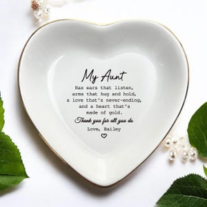 May include: A white heart-shaped ceramic trinket dish with a gold-toned rim. The center features black text: My Aunt, Has ears that listen, arms that hug and hold, a love that's never-ending, and a heart that's made of gold. Thank you for all you do, Love, Bailey.