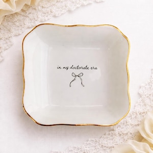 May include: A set of three ceramic mugs with a speckled, matte finish. The mugs are in shades of cream, light grey, and dark grey. Each mug has a simple, minimalist design, ideal for coffee or tea.