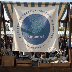 Könnte beinhalten: Ein Marktstand im Freien zeigt ein Banner mit dem Text "A Center for Practice, Presence, & Purpose" und dem Wort "kinward" in Weiß. Das Banner hat ein blaues und grünes kreisförmiges Logo. Holzkisten zeigen verschiedene Artikel.
