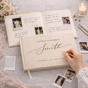 May include: A cream-coloured wedding guest book with the names "Stephan & Georgia Smith" and the date "October 15, 2026 - Ibiza, Spain" on the cover. The book is open, with handwritten notes and photos.