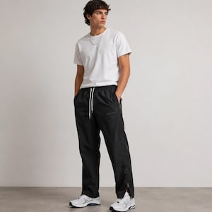 May include: A person wearing a white crew neck t-shirt and black track pants with a white drawstring. The pants have a zipper detail at the ankle and are paired with white sneakers. The outfit is casual and sporty.