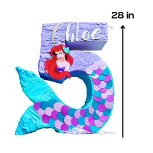 May include: A number 5 pi&ntilde;ata in the shape of a mermaid, 28 inches tall. The pi&ntilde;ata is decorated with blue, purple, and pink scales. It features a mermaid illustration and the name "Chloe" in cursive.