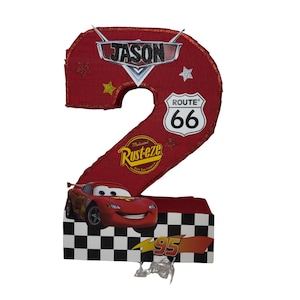 May include: A red number 2 piñata with a Cars theme. The piñata features the name "Jason", Route 66, and the number 95. A cartoon image of Lightning McQueen is on the front. The base of the piñata has a black and white checkered pattern.