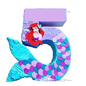 May include: A number 5 pi&ntilde;ata in the shape of a mermaid tail, featuring a cartoon mermaid with red hair and a purple top. The tail is decorated with blue, purple, and pink scales. The top of the pi&ntilde;ata has a blank purple rectangle.