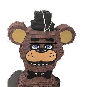 May include: A brown paper piñata in the shape of a bear with a black top hat and bow tie. The bear has tan ears, a tan muzzle, and blue eyes. A white string is attached to the top of the hat.