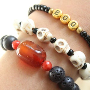 May include: Three bracelets with a Halloween theme. One bracelet has the word "BOO" spelled out in gold beads. Another has white skull beads. The third bracelet has black lava beads and a large orange bead.