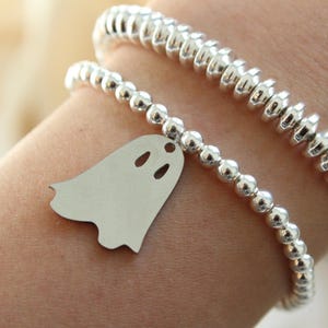 Op de afbeelding: Zilveren armbanden met kralen en een spookbedel. Eén armband heeft kleine ronde kralen, de andere heeft grotere, geribbelde kralen. De spookbedel heeft twee oogjes en een mond.