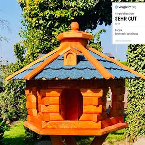 Könnte beinhalten: Ein Vogelhaus aus Holz mit einem blauen Schindeldach und einem sechseckigen Sockel. Das Vogelhaus ist orange lackiert und hat eine kleine Öffnung, durch die Vögel eintreten können. Das Vogelhaus steht auf einem Holzpfahl.